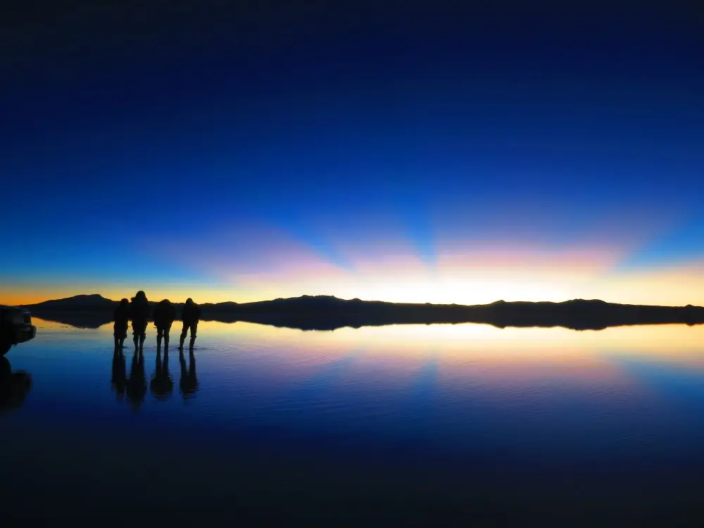 ウユニ塩湖の夜明け、太陽の光芒と人々のシルエット