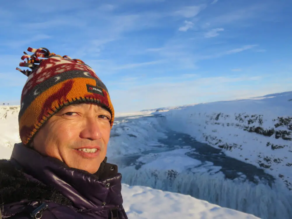 雪景色を背景に、冬の帽子を被った人物がグトルフォスの滝を眺めている。