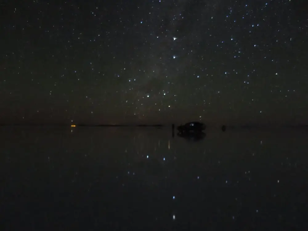 ウユニ塩湖の水面に満天の星空が映り込む、神秘的な夜の光景。