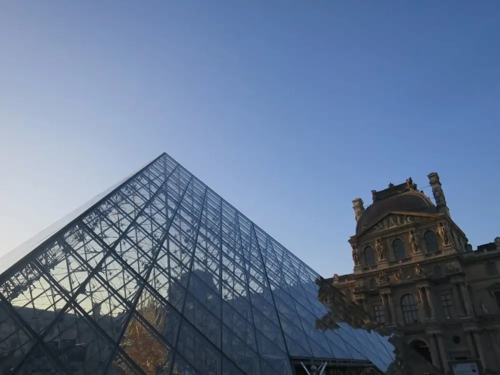 青空に映えるルーブル美術館のガラスのピラミッドと歴史的建築物。