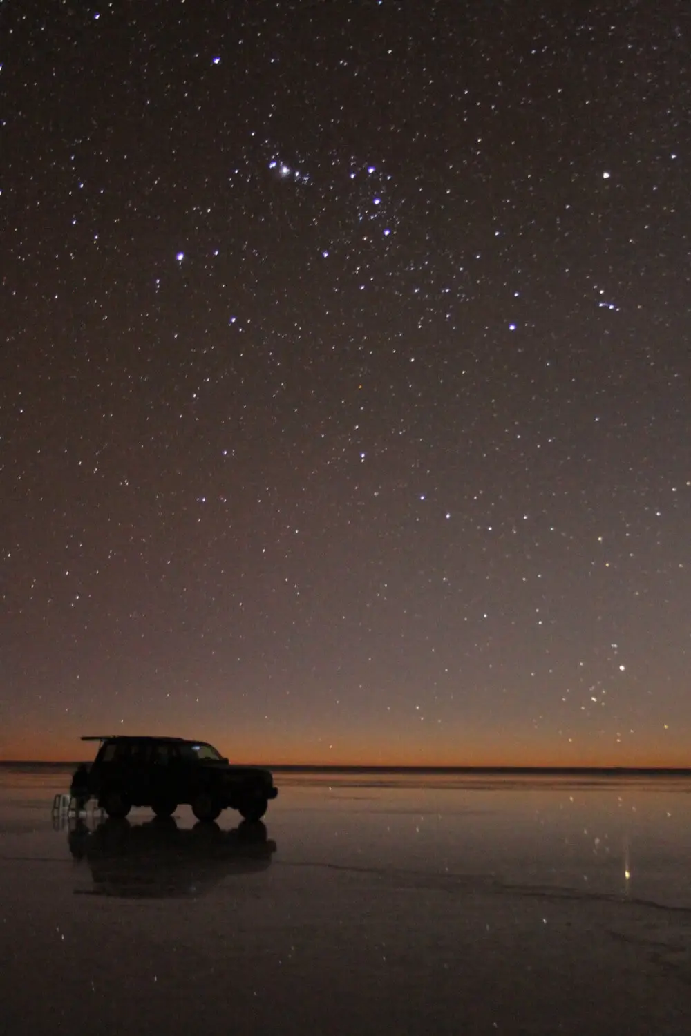 ウユニ塩湖の湖面に映る4WD車と満天の星空