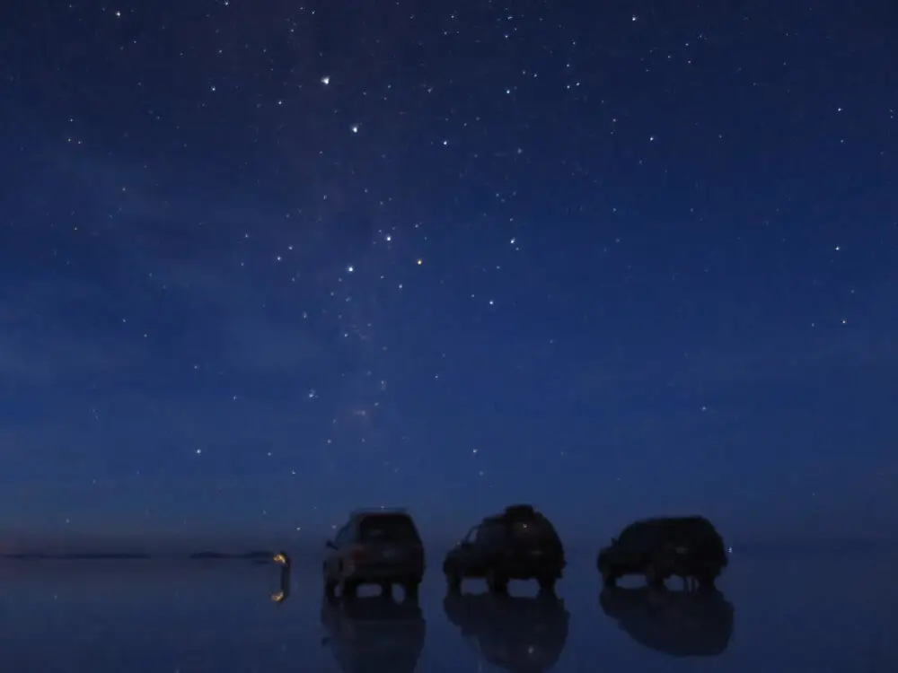 星空の下、ウユニ塩湖の湖面に三台の4WD車が映る光景