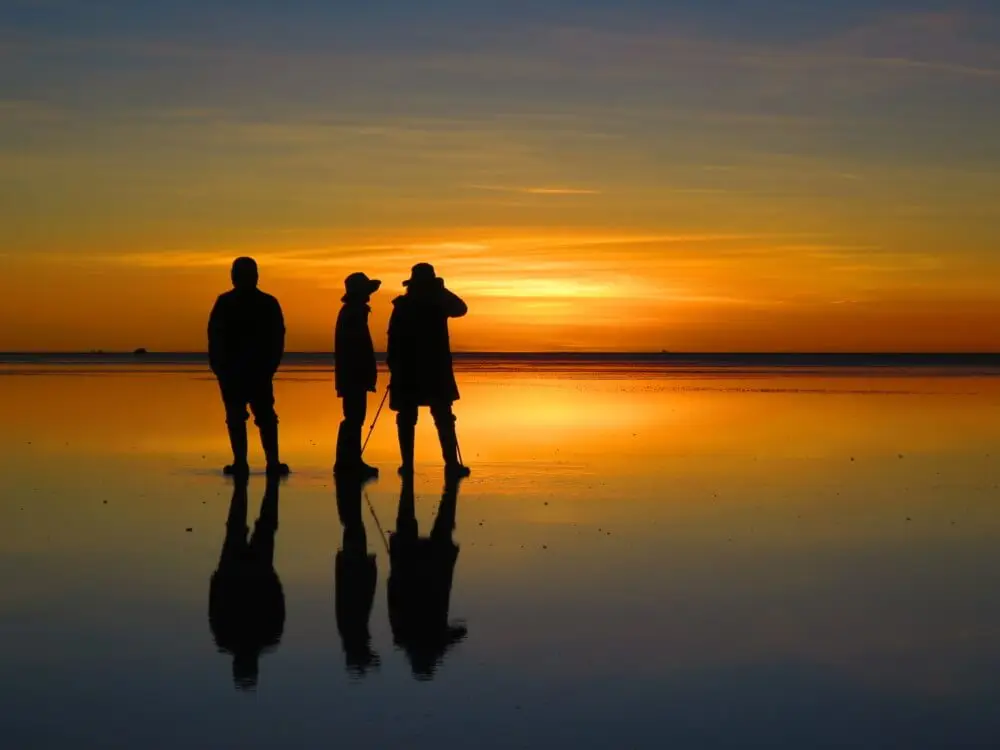 ウユニ塩湖で夕陽を眺める3人の人物のシルエット