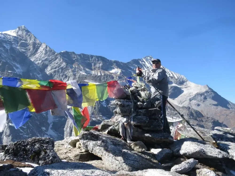 パラクピーク山頂でタルチョーがたなびく横に立つ登山者