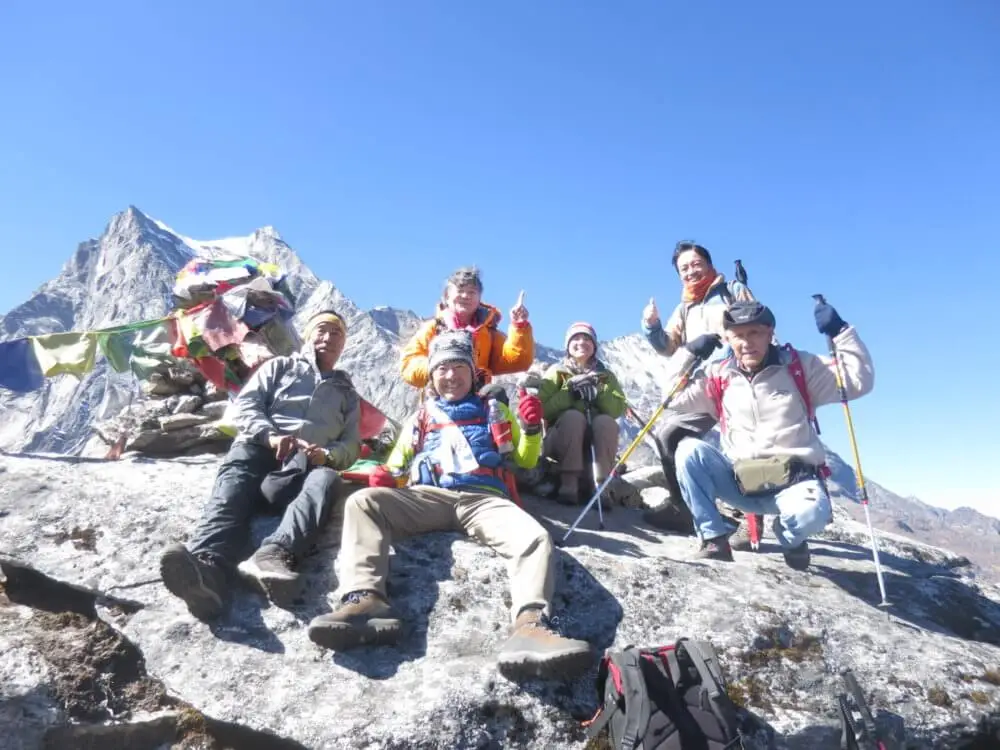 パラクピーク山頂で、雪山を背景に登山隊が休憩している。