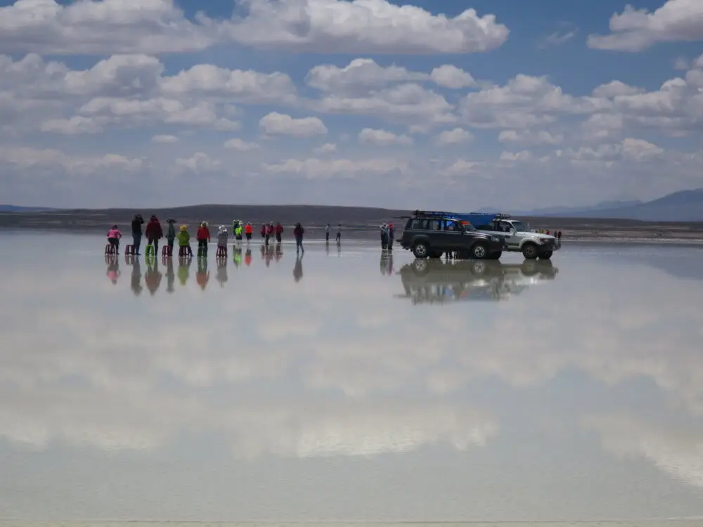 ウユニ塩湖の水面に長靴で立つ人々、その隣に停まる4WD車