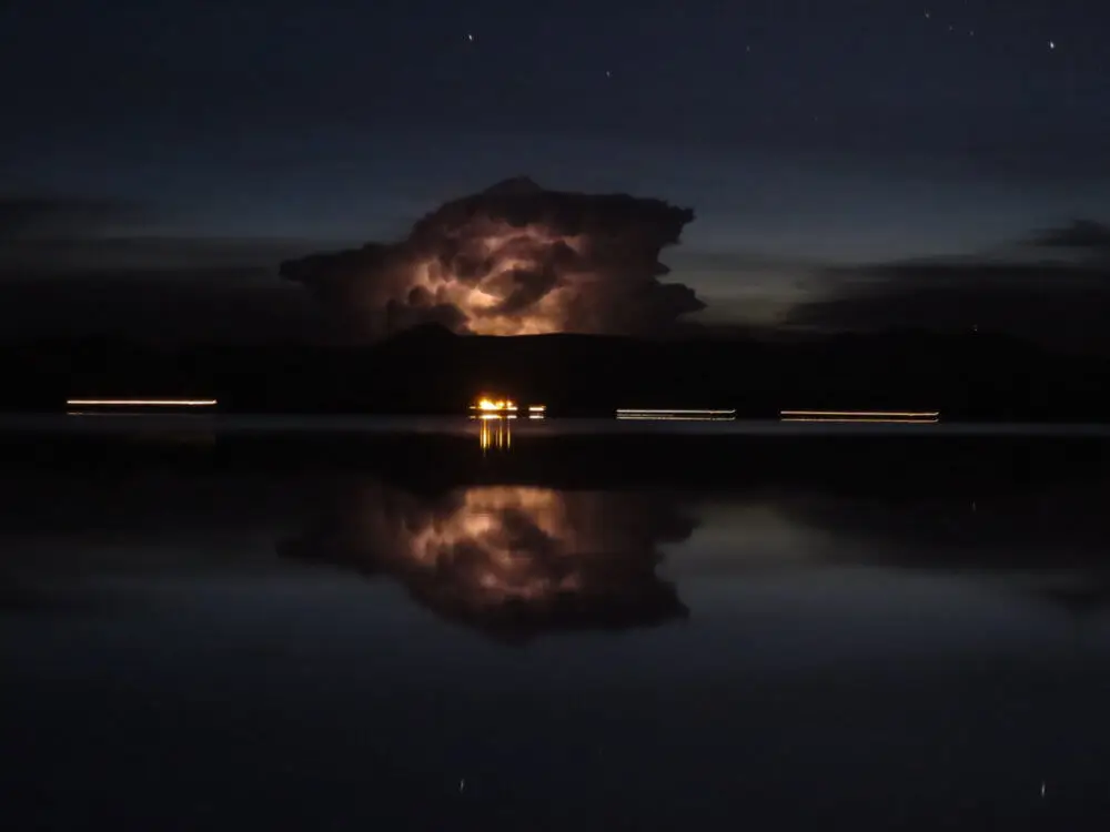 夜のウユニ塩湖に、遠くで光る雷雲とその反射が広がる。