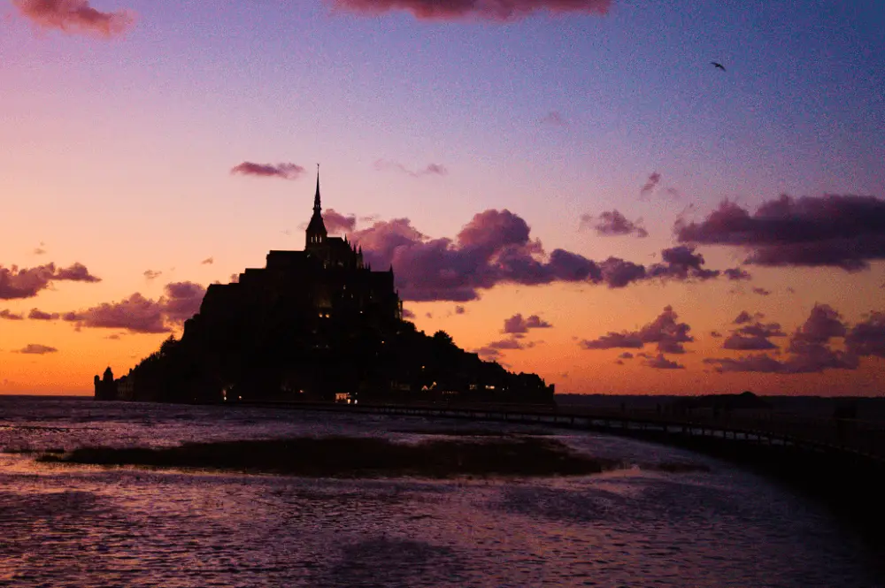 夕焼けに染まる空を背景に、モンサンミッシェルがシルエットで浮かぶ