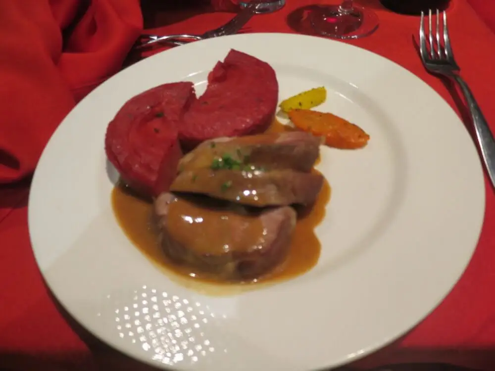 濃厚なソースがかかった肉料理と、赤やオレンジ色の付け合わせが添えられた皿。