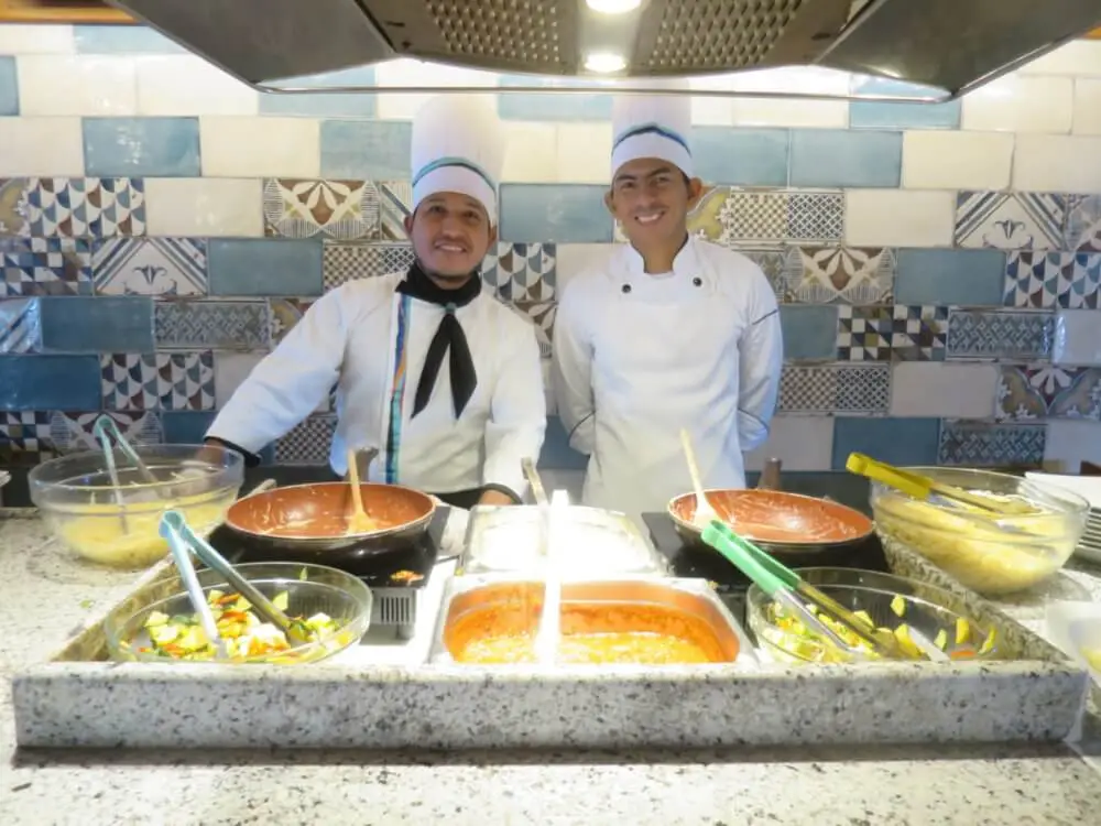 クルーズ船ビュッフェカウンターで、笑顔で料理を準備する2人のシェフ。