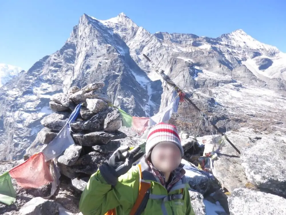 パラクピークの山頂にある石積みとタルチョーを背景にした人物。