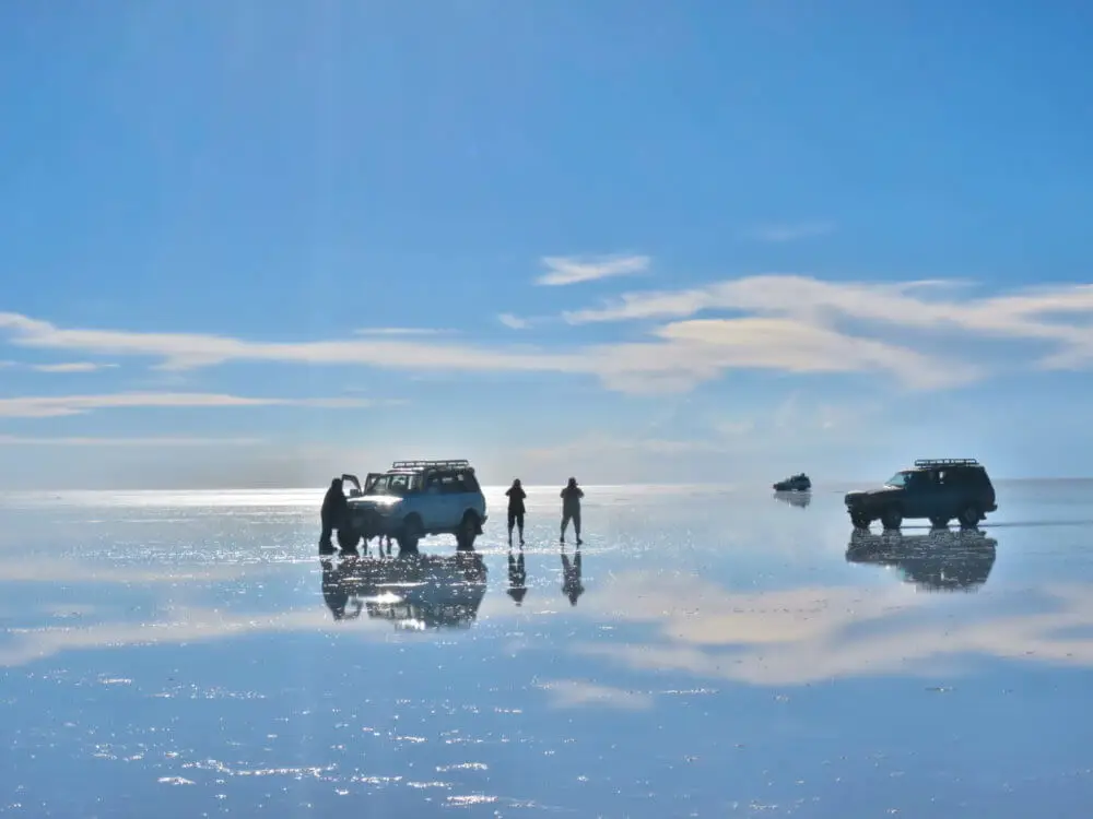 ウユニ塩湖の水面に立つ人々、4WD車、そして空の雲の反射