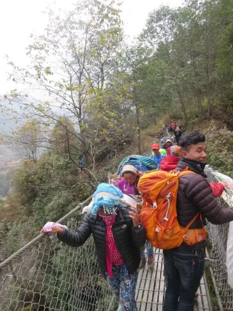 吊り橋を渡るトレッカーたち。多くの荷物を運ぶ人々。