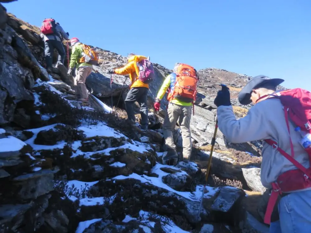 雪が残る岩だらけの急坂を登る登山者たち。