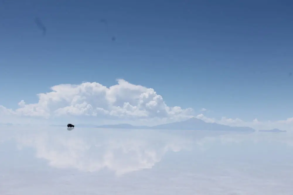 ウユニ塩湖の広大な水面を進む一台の4WD車と雲の反射
