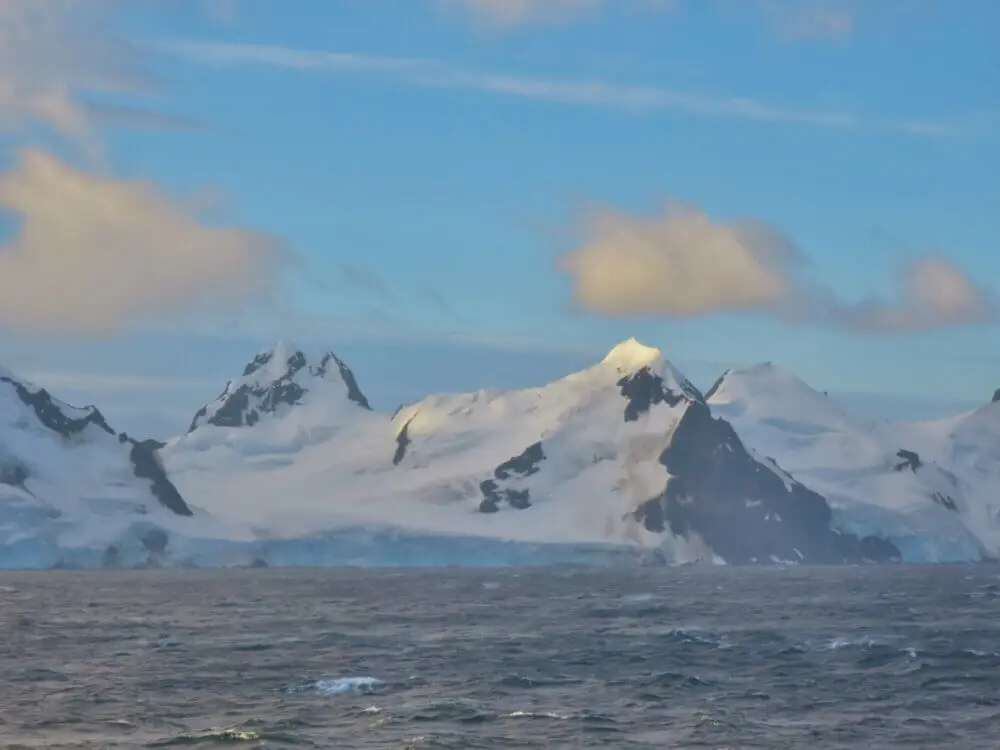 南極の雪山と波立つ海、青空に白い雲