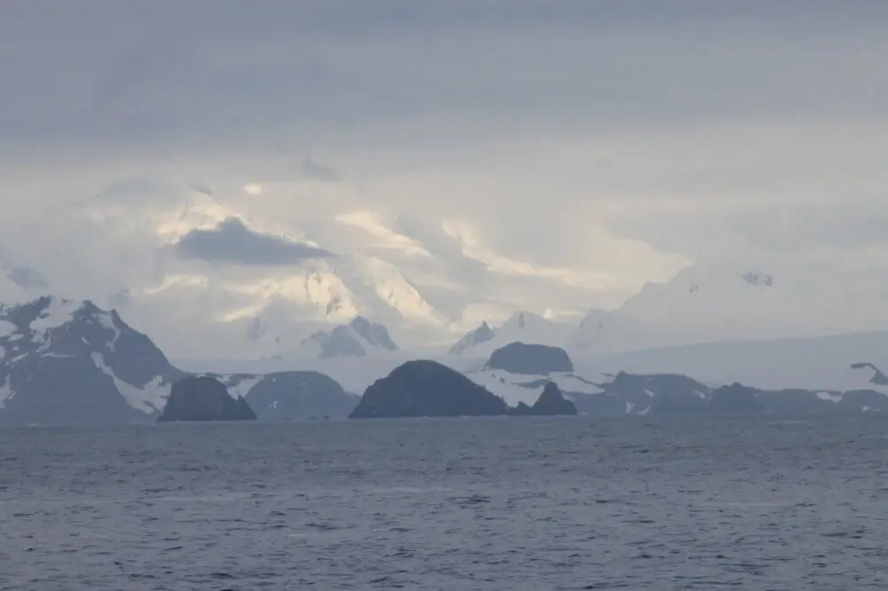 曇り空の下、南極の雪山と岩場の島々が遠くに見える