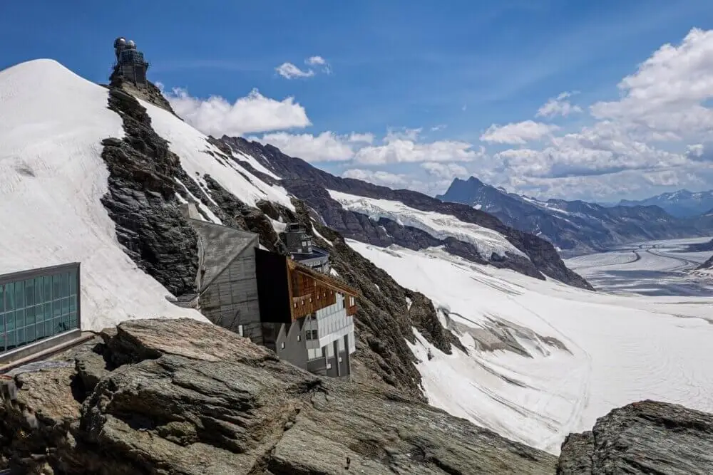 雪をまとったスイスの山岳に建つ天文台と氷河の眺望