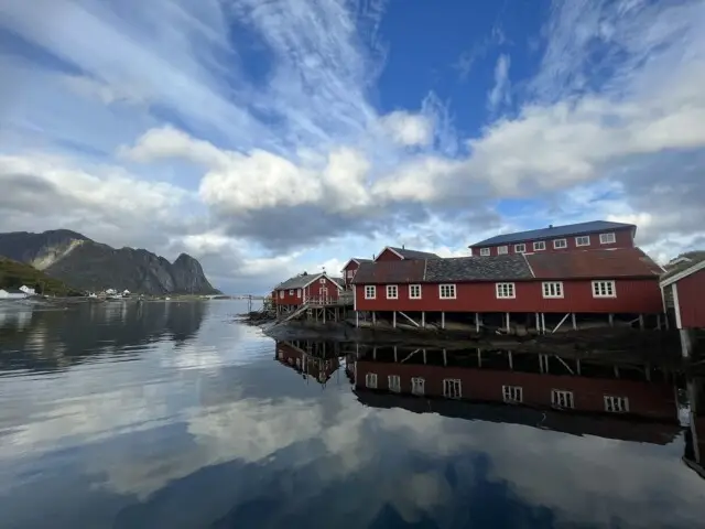 赤い漁師小屋が水面に映るノルウェーのフィヨルド風景。