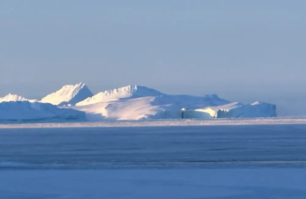 広大な氷の海に浮かび、陽光を浴びて輝く巨大な氷山群。