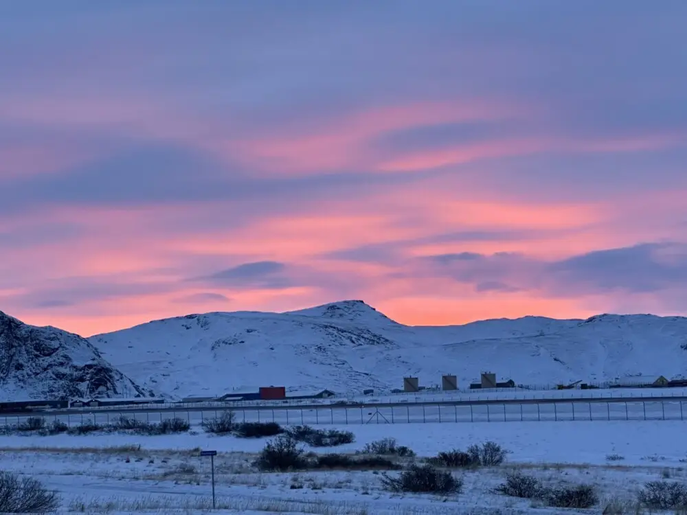 雪に覆われた山並みを背景に、ピンク色に染まる幻想的な夕焼け空。