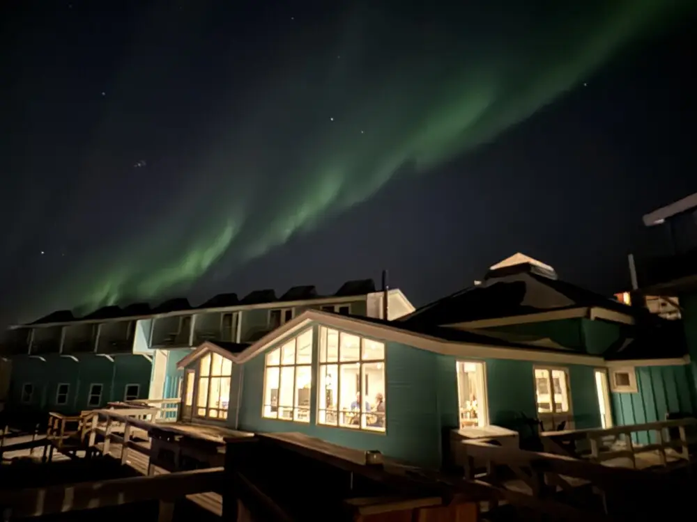 ホテルの建物群の夜空に緑色のオーロラが輝く。